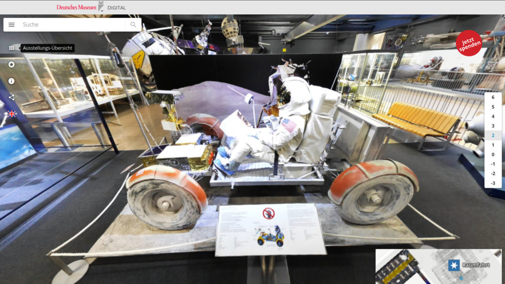 Ein Fahrgestell mit Astronauten im weißen Anzug. Schwarze, staubige Ballonreifen sind mit orangefarbenen Schutzblechen umhüllt. Kein Dach. Zu sehen auf dem Virtuellen Rundgang des Deutschen Museums München.